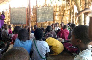 A large number of children learning lessons in a makeshift classroom.